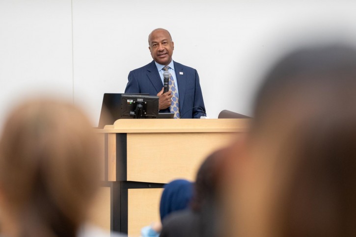 Gary May stands at a podium, addressing an audience sitting in front of him.