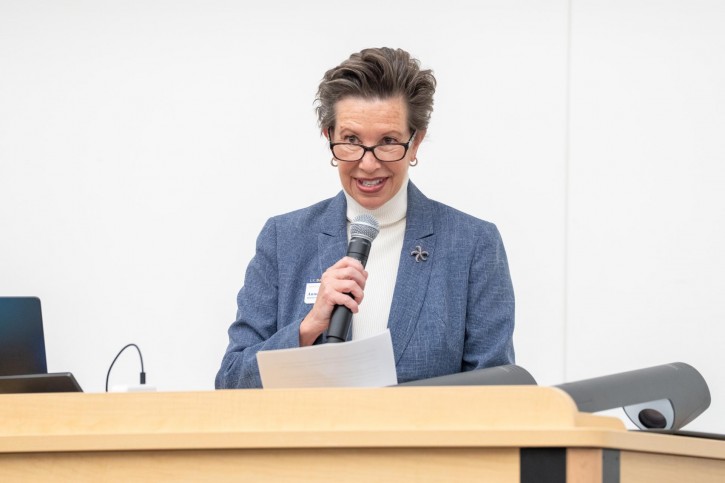 Anne Jones stands at a podium, addressing an audience sitting in front of him.