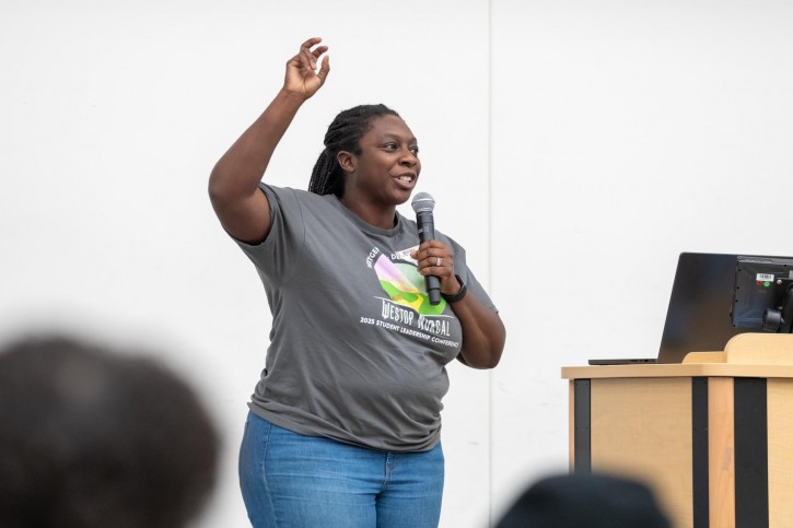 One of the event organizers stands on stage with her arm raised, speaking into a microphone.