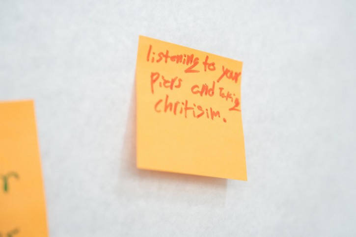 A close up of a sticky note that says "listening to your peers and taking criticism."