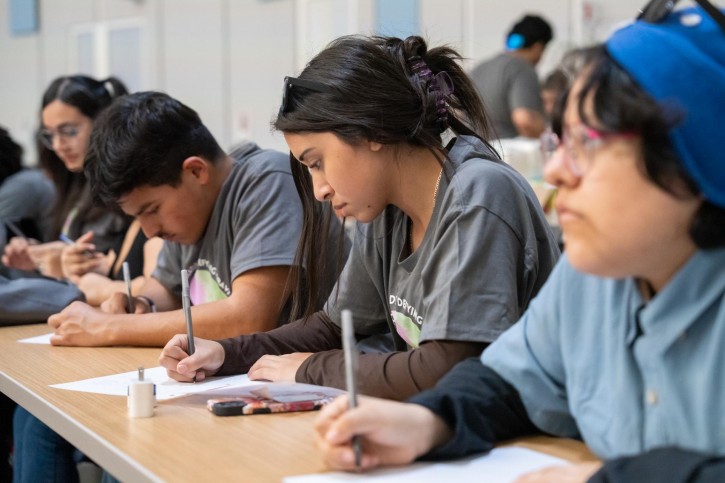 Four students look down at the paper in front of them, writing.