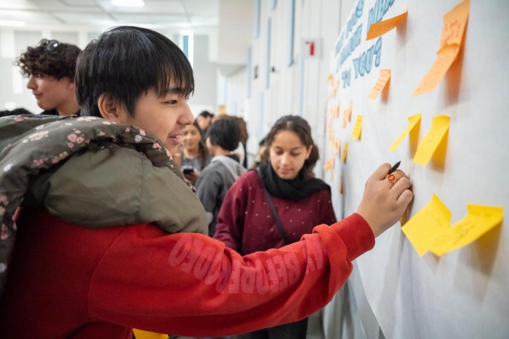 Students place sticky notes on a white board.