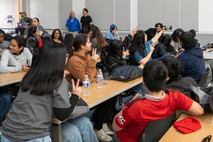 A group of students lean over desks to pose in a selfie being taken.