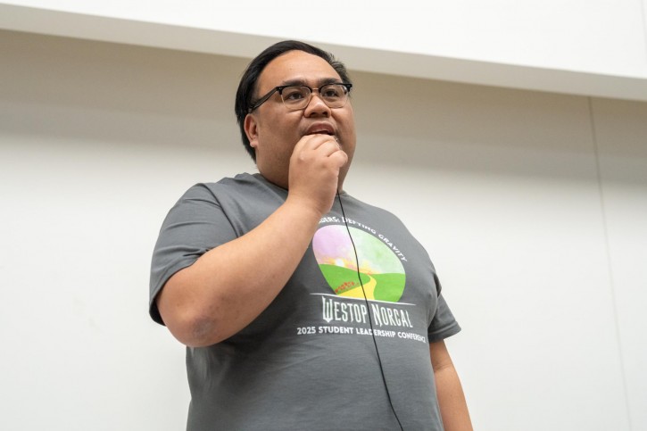 One of the event organizers stands on stage, speaking into a microphone.