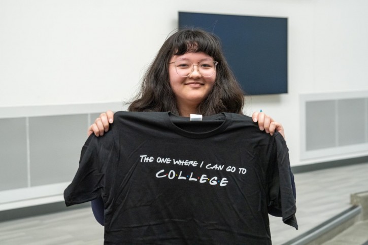 A girl holds up a t-shirt that says "The one where I can go to college."