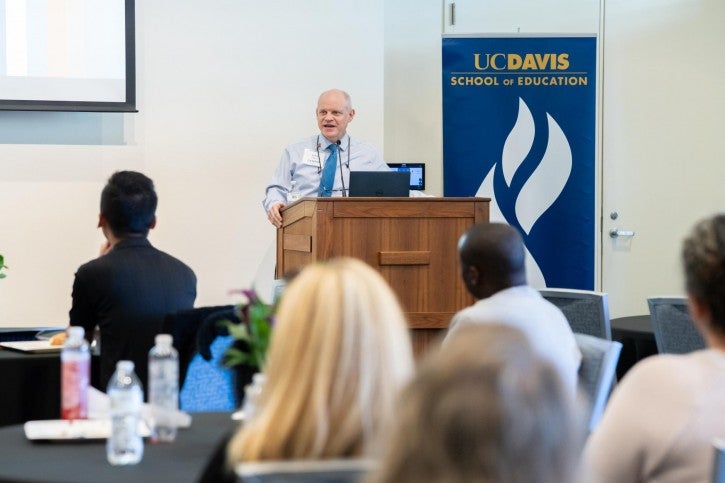 Alumnus John Pellman stands at a podium and addresses the audience.
