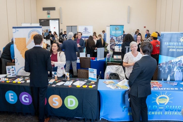Tables lined up in rows throughout a room, with students speaking to hiring managers.