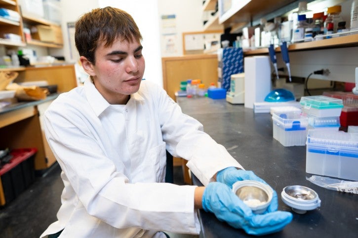 Student wearing gloves and white lab coat displays lab dish