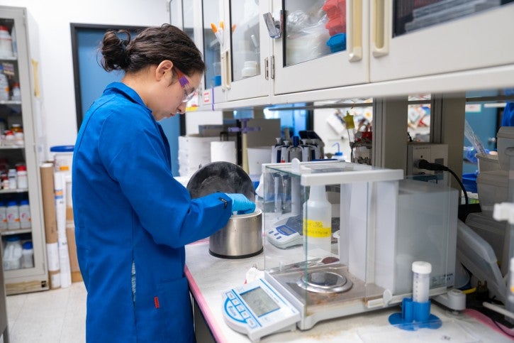 Student wearing gloves and blue lab coat works at lab station