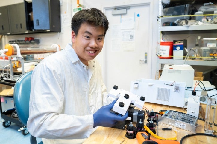 Student wearing gloves and white lab coat works at lab station