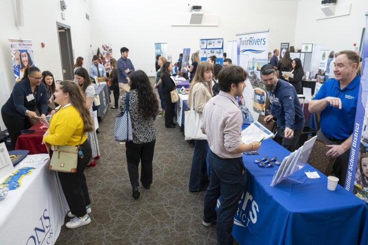 A bustling career fair with diverse professionals interacting at exhibitor tables. Attendees engage in vibrant conversations, exchanging brochures and ideas.