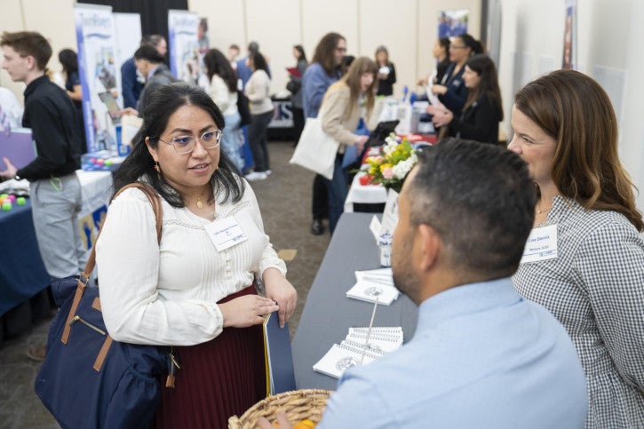 A woman speaks with two recruiters at a career fair.
