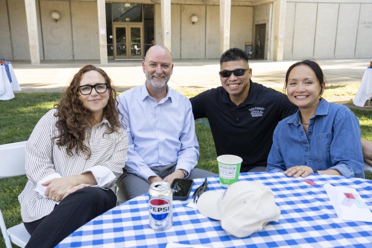 Michal Kurlaender sits at a table and poses for a photo with three CANDEL students.