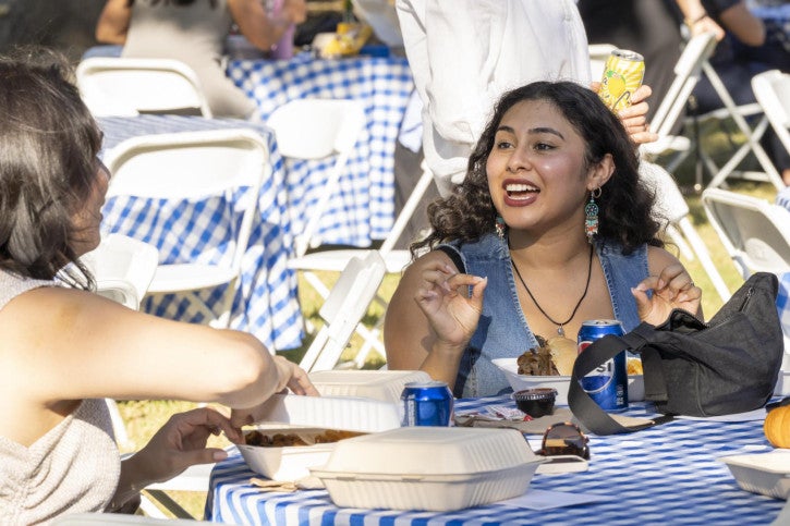 A PhD student sits at a table and speaks to another attendee.