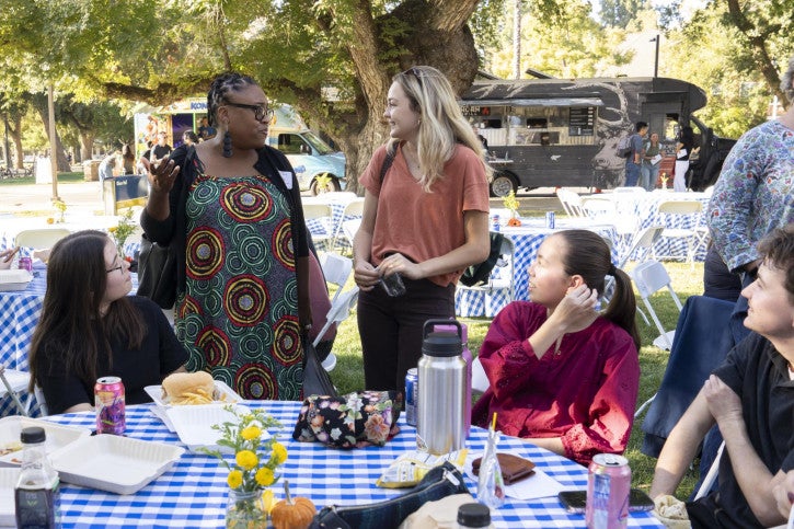 Taylor Ferdinandsen and Alexis Patterson Williams stand amongst the picnic tables and speak to each other.