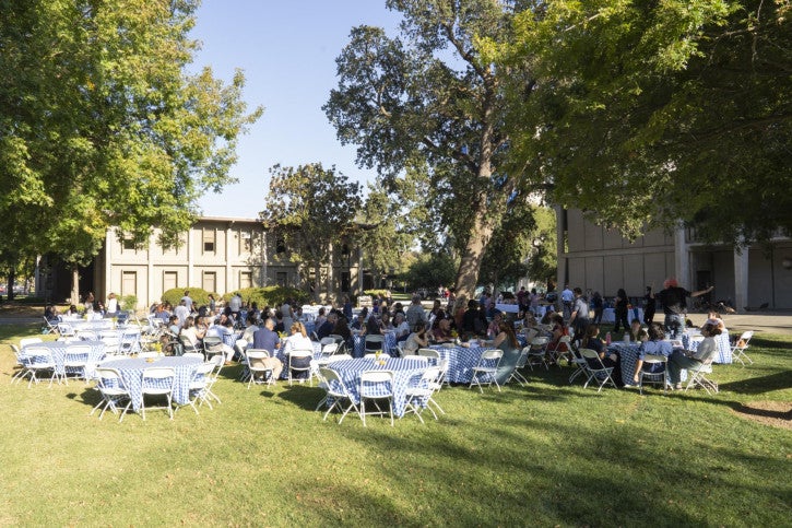 Round tables with blue gingham tablecloths sit on Olson Lawn, outside the School of Education building.