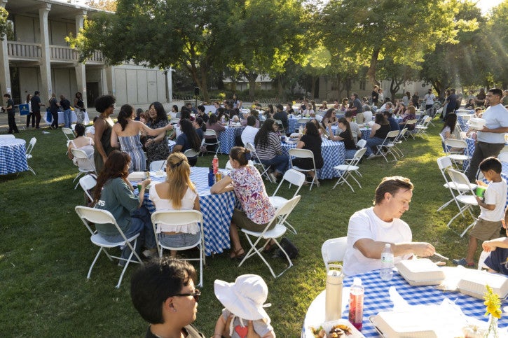 Attendees gather at round tables covered with blue gingham tablecloths.