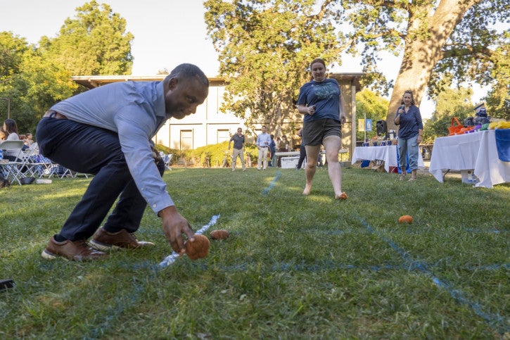 Darnel Degand reaches down to place a marker on an oversized tic-tac-toe board. A student runs up behind him.