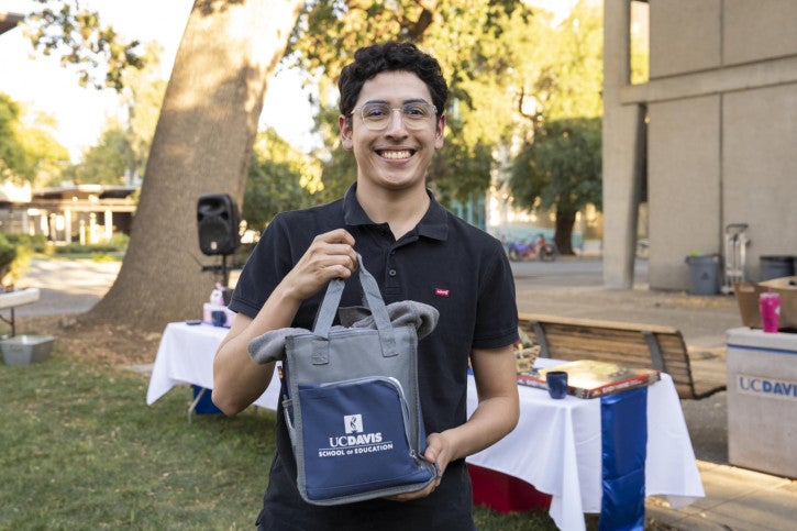 A raffle winner holds up a School of Education lunchbox full of branded merchandise.