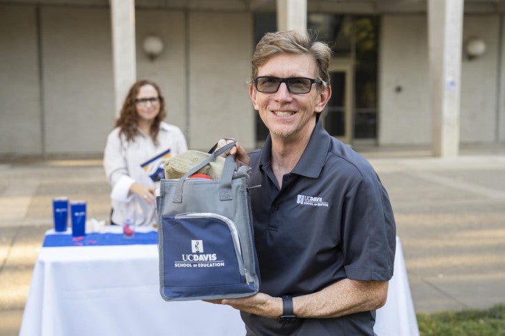 Tom Smith, a raffle winner holds up a School of Education lunchbox full of branded merchandise.