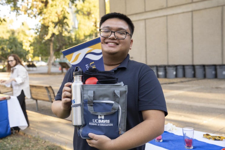 A raffle winner holds up a School of Education lunchbox full of branded merchandise.