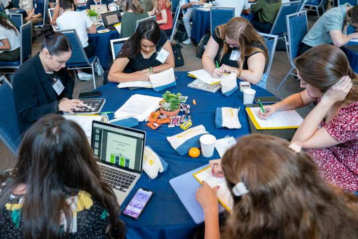 Students sit around a table, writing.