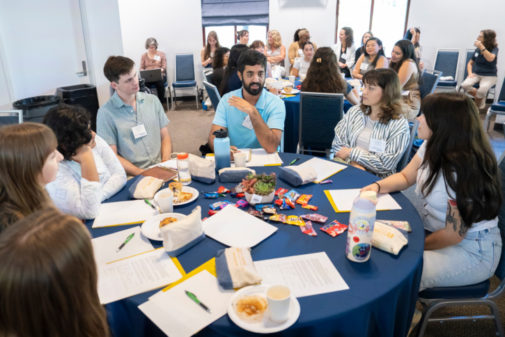 Students sit at a round table, talking.