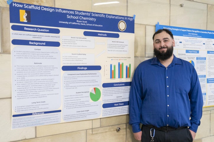 A man in a blue shirt stands next to a research poster titled "How Scaffold Design Influences Students' Scientific Explanations in High School Chemistry." 