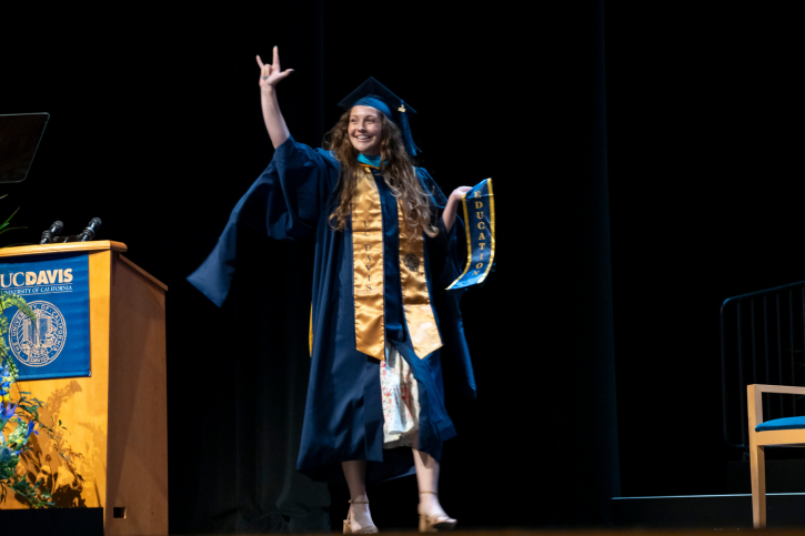 An MA grad holds up the "I love you" sign as she crosses the stage.