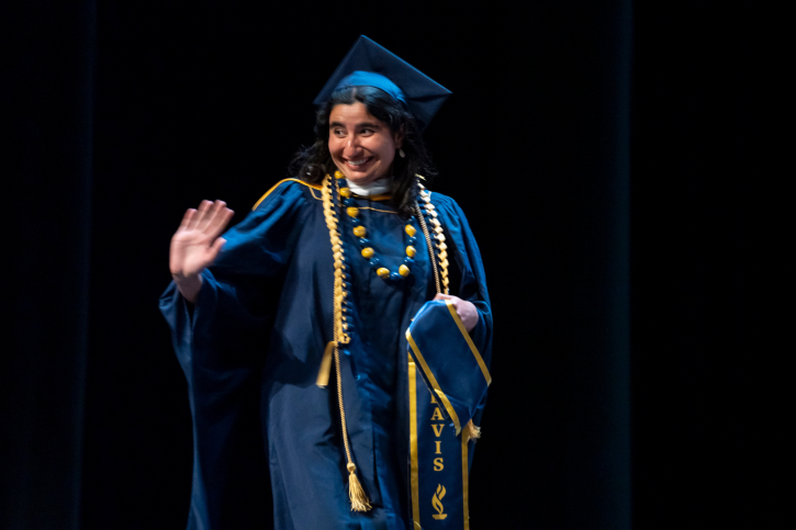 MA grad Riya smiles and waves as she crosses the stage.