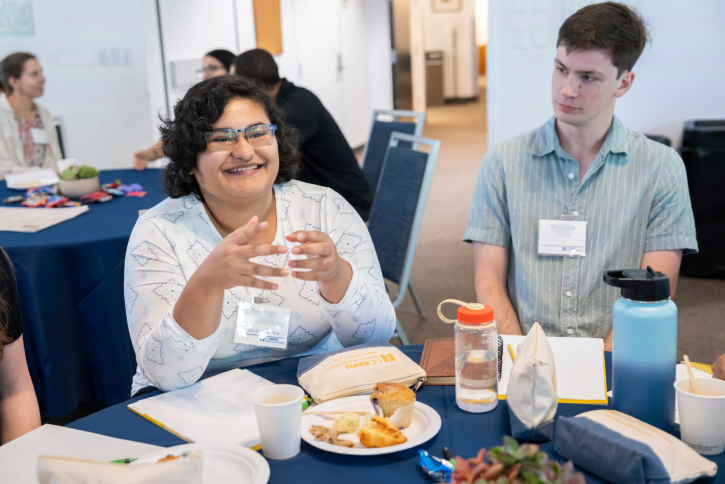 A student smiles and speaks to the others at her table. Next to her, another student listens intently.