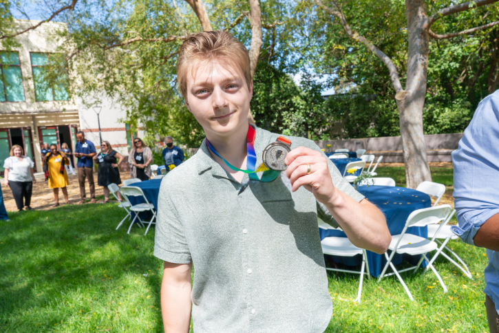 A student with blond hair holds up his silver medal.