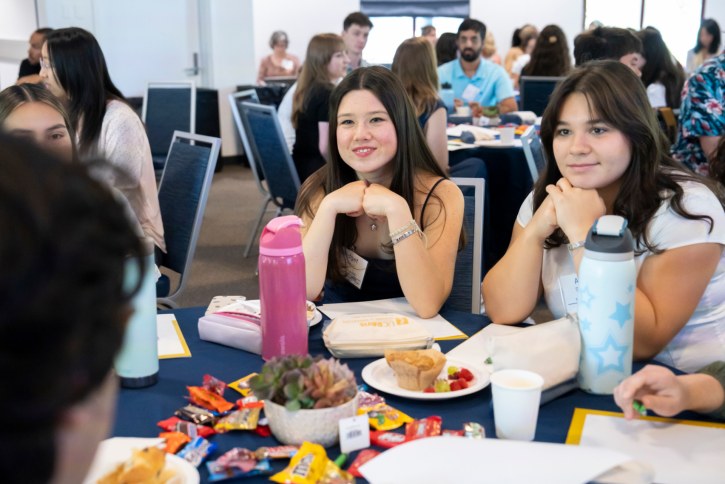 Students listen to someone off-camera, smiling.