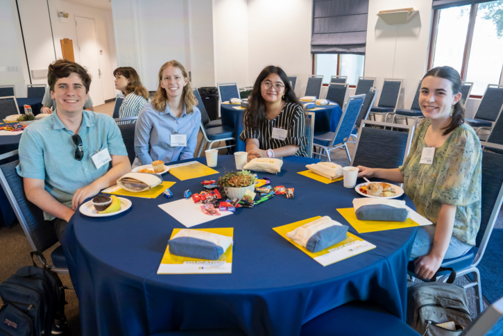Students sit at a table and smile for the camera.