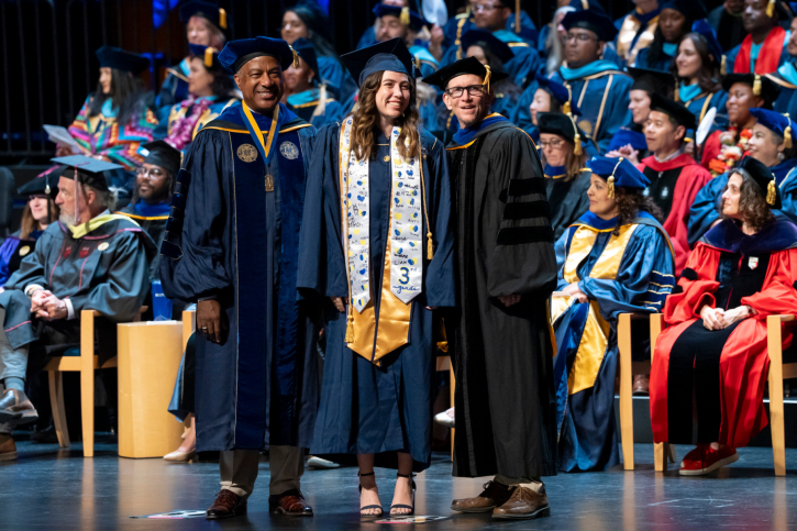 A credential grad smiles with Chancellor May and Dean Smith.