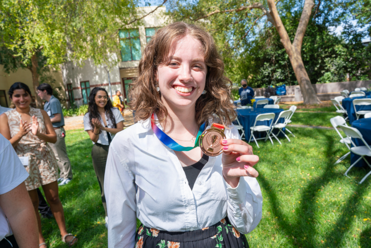 A student with curly hair holds up her bronze medal.