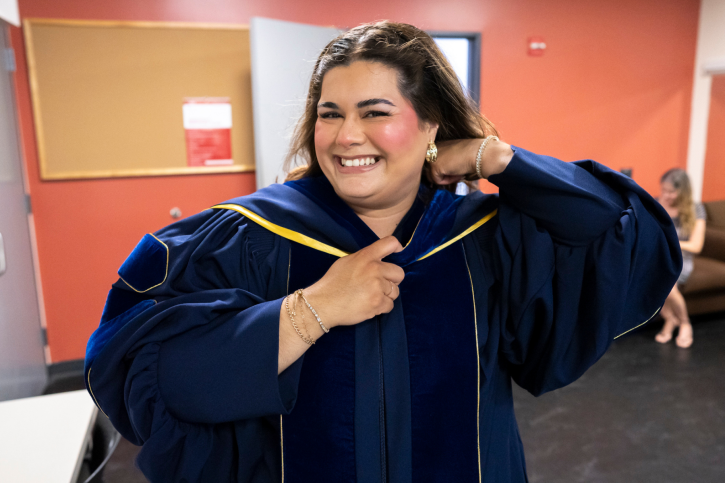 A graduate student smiles as she dons her regalia.