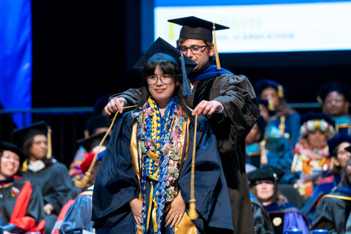 A credential student wearing many leis receives their cord.