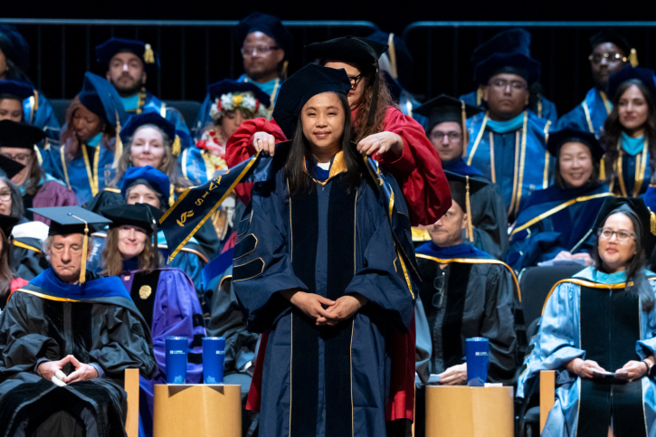 A PhD grad smiles as she receives her stole.