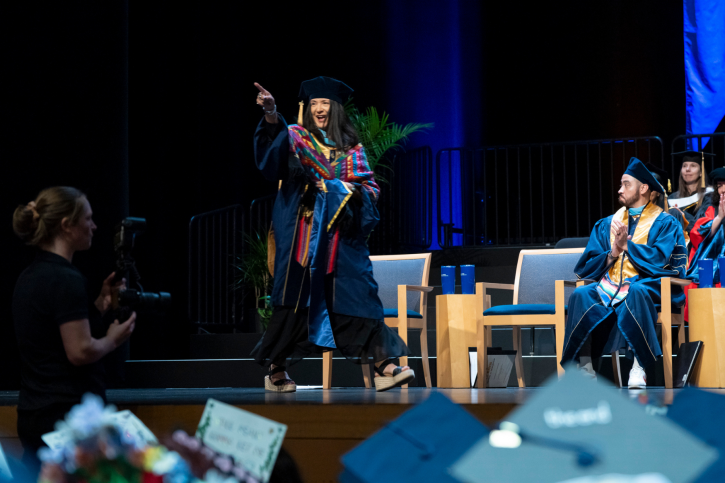 An EdD grad smiles and points to the audience as she crosses the stage.