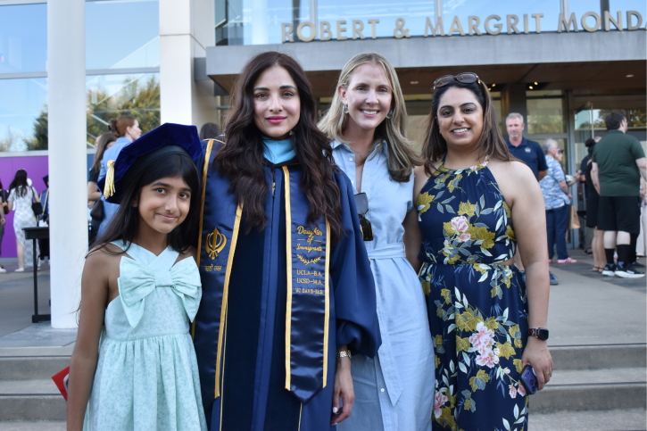 A doctoral graduate smiles, standing with friends and family.