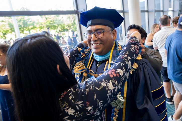 A doctoral grad smiles as someone puts a lei on him.