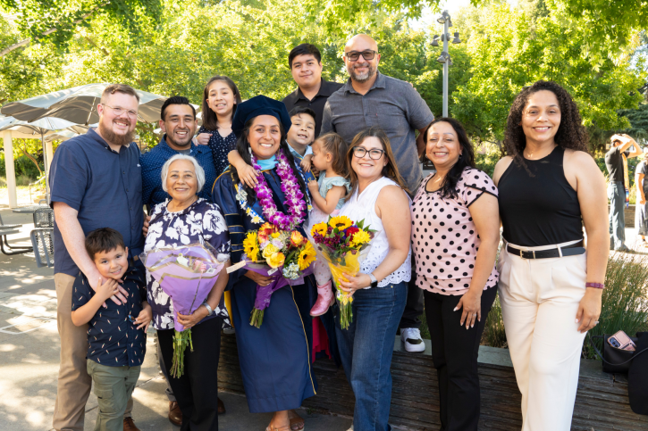 A doctoral grad smiles, surrounded by many family members.