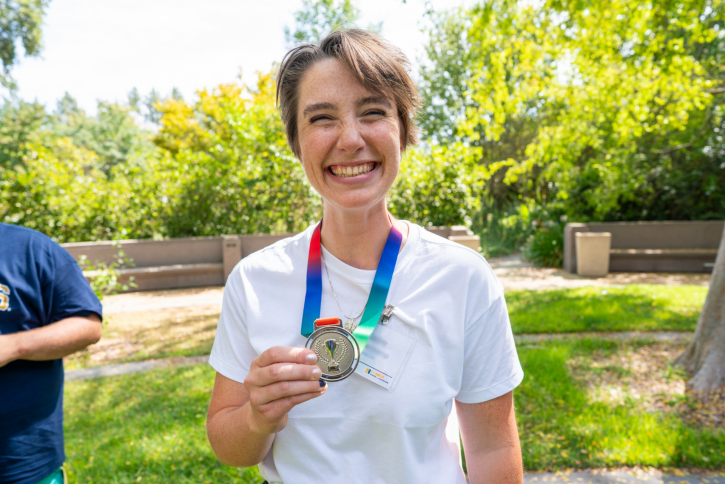 A student with short hair smiles widely while holding up her silver medal.