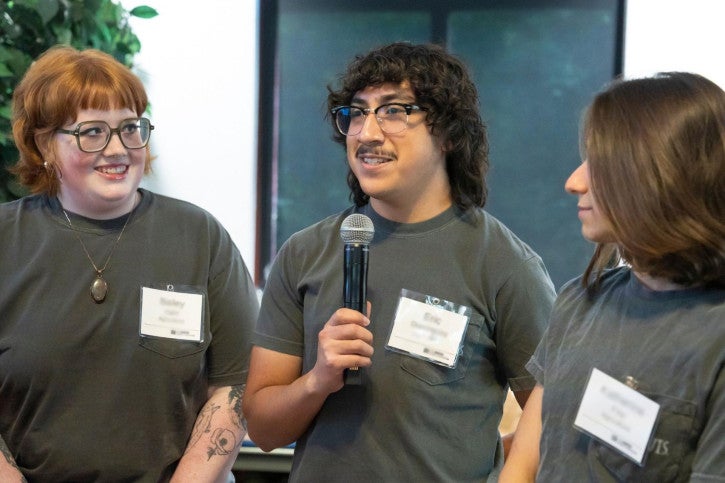Three agriculture credential students stand at the front of the room and speak into a microphone.