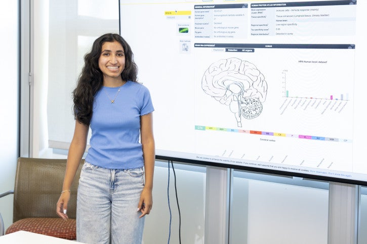 Amaira stands next to a screen presenting data and smiles.