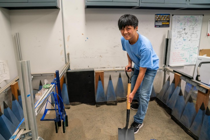 Anson holds a shovel while standing on sand.