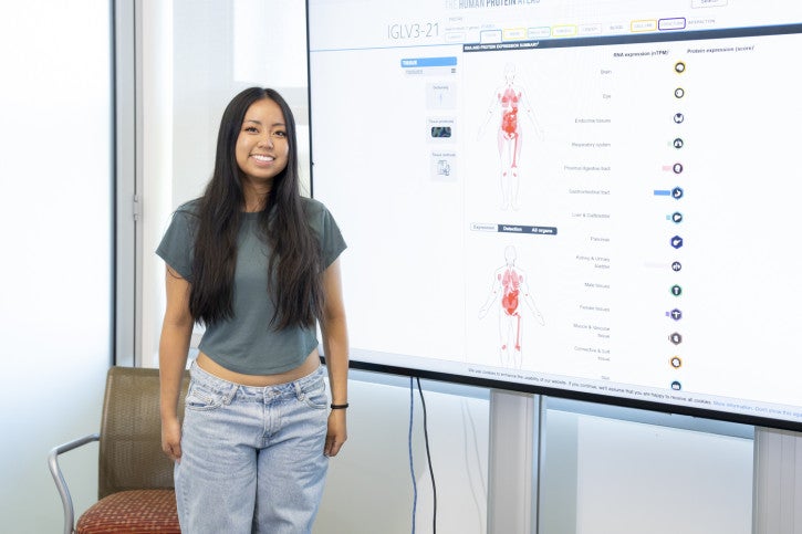 Claire smiles next to a screen showing research data.