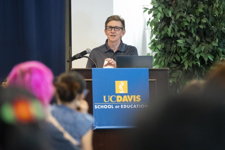 Dean Tom Smith stands at a podium and addresses the audience seated in front of him.