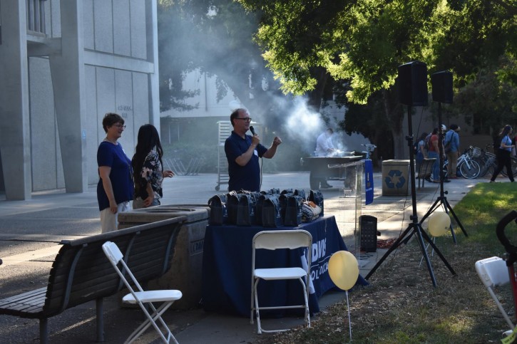 People speak at microphone with BBQ behind them